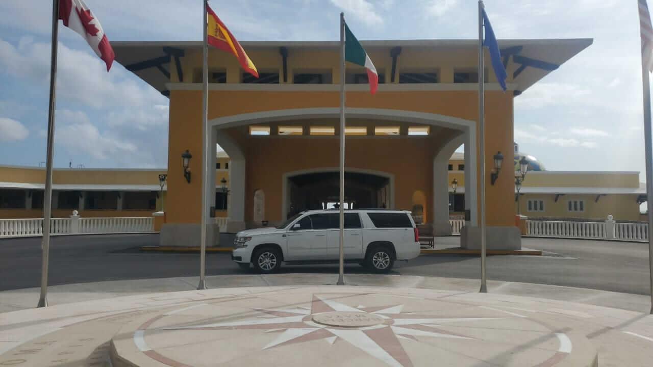 Camioneta blanca de lujo estacionada frente a lobby de hotel con banderas 